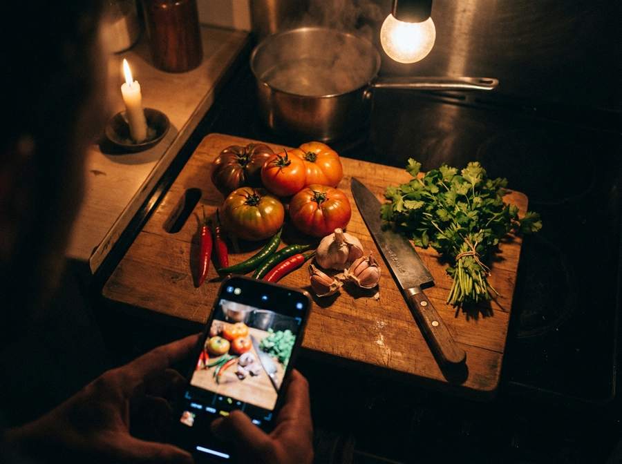 A phone photographing a board of tomatoes, chillies, garlic and coriander in a dark kitchen — the ingredients for a post.